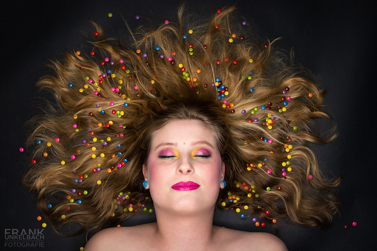 Bunt geschminkte Frau mit farbigen Smarties in den ausgebreiteten Haaren (Portrait)