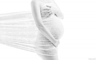 High-key Aufnahme einer schwangeren Frau. Der Babybauch wird von einem weißen Tuch mit Netzmuster umhüllt.