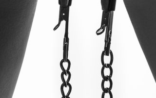 Frau trägt zur Züchtigung Klemmen an ihren Schamlippen. An den Klemmen wurden zusätzlich kleine Gewichte angebracht.